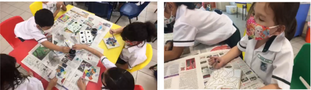 Young students in white uniforms and face masks doing an art activity at a table covered with newspaper.